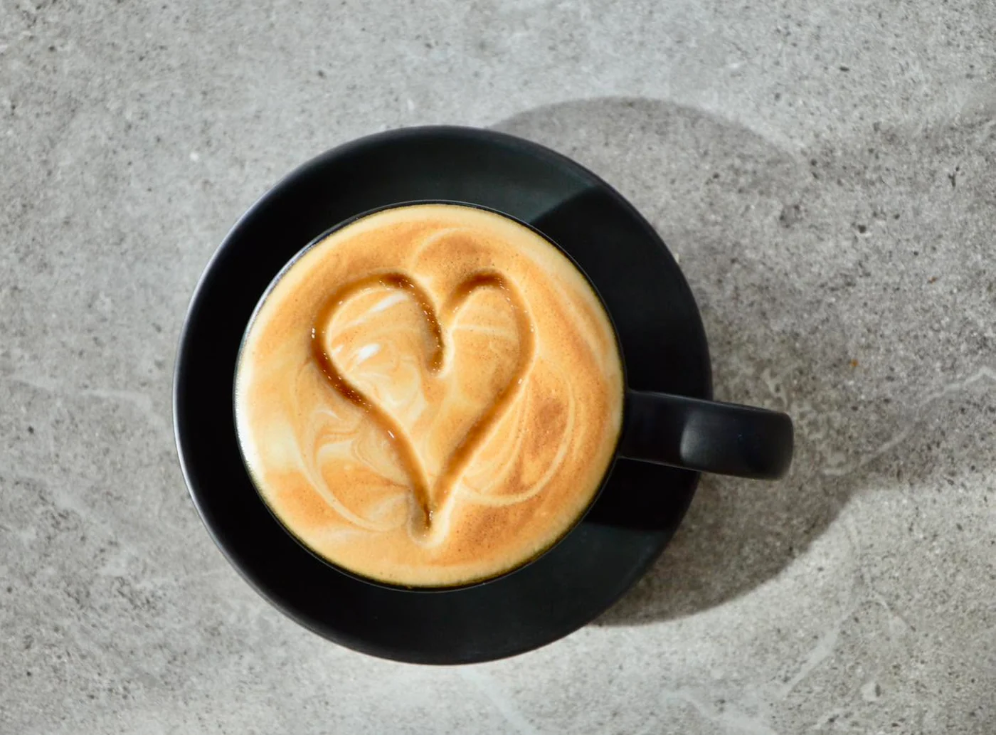 Heart-shaped latte art in a black coffee cup at O’NO